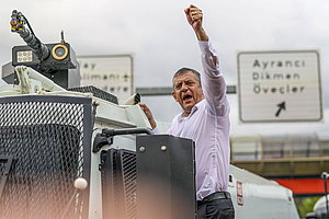 Özgür Özel steht auf einem Wasserwerferfahrzeug der Polizei, hält eine Rede und hebt die linke Faust in die Höhe.